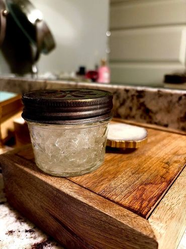 Small jar with a metal lid on a wooden tray in a bathroom setting.