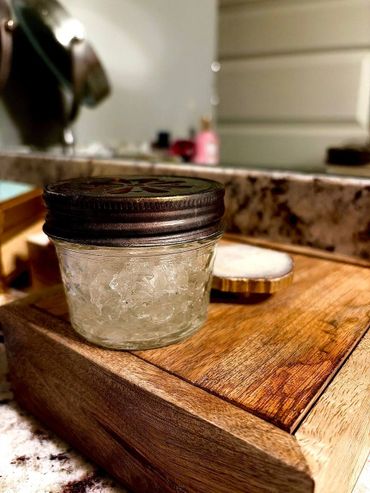 Small jar with a metal lid on a wooden tray in a bathroom setting.