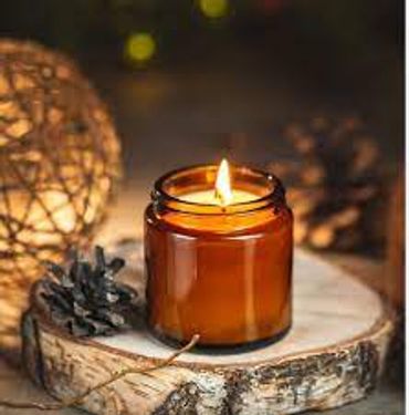 Lit candle in amber jar on wooden slice with pinecones for cozy ambiance.