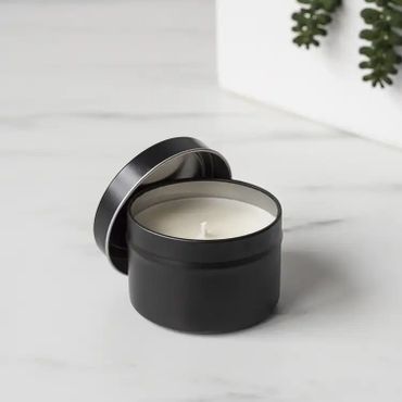 Black tin candle with lid on a white surface.