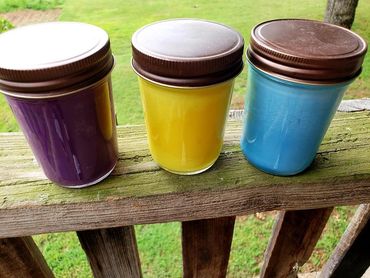 Three jars with colorful contents and brown lids on a wooden railing.