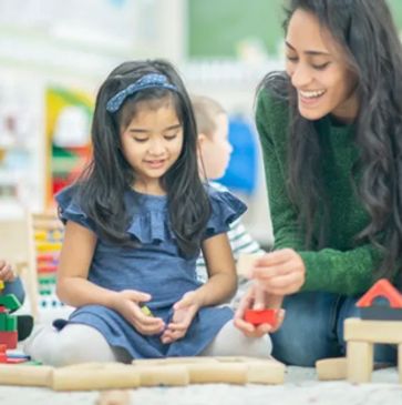A teacher and children playing with building blocks in a classroom.