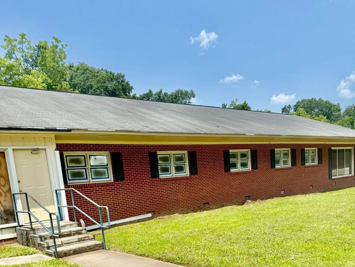Red brick building with multiple windows and a grassy lawn under a clear sky.