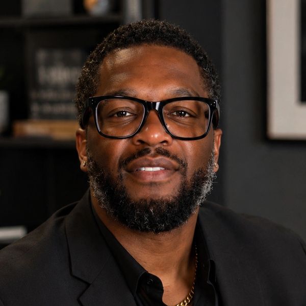 Man with glasses and beard in a black suit.