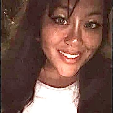 A woman smiling warmly at the camera in dim lighting.