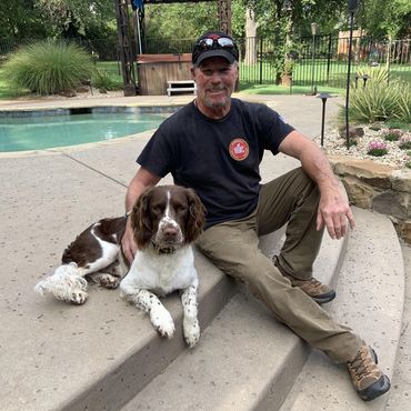 Man sitting on steps with a brown and white dog by a backyard pool.