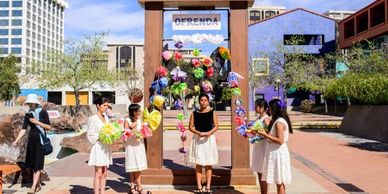 Young women standing with paper marcher flowers, a Barrio Stories Installation theatre vignette.