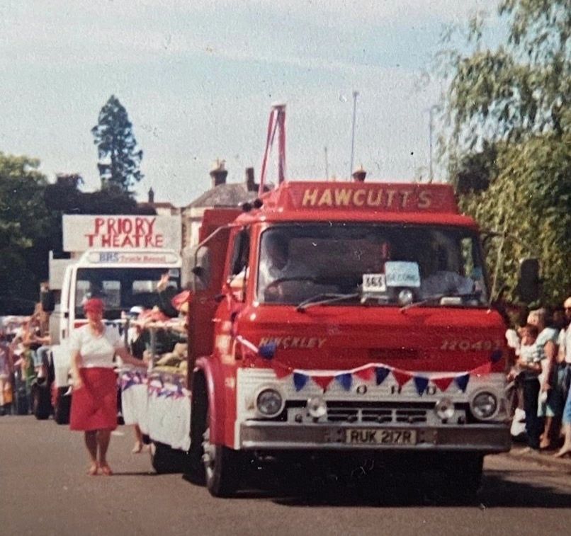 A vintage red HAWCUTTS truck decorated with bunting in a parade.