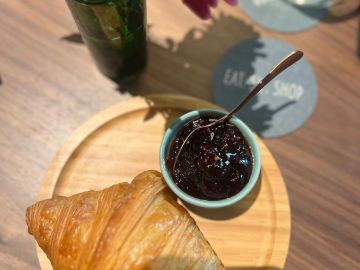 Croissant and jam served on a wooden plate with a spoon.