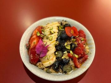 A vibrant bowl of granola topped with banana, strawberries, blueberries, and edible flowers.