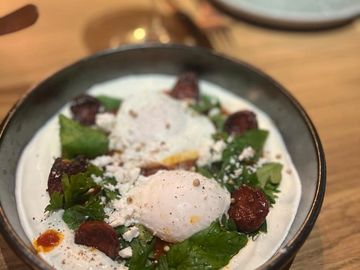 Poached eggs on a bed of greens with creamy sauce and sausage slices.