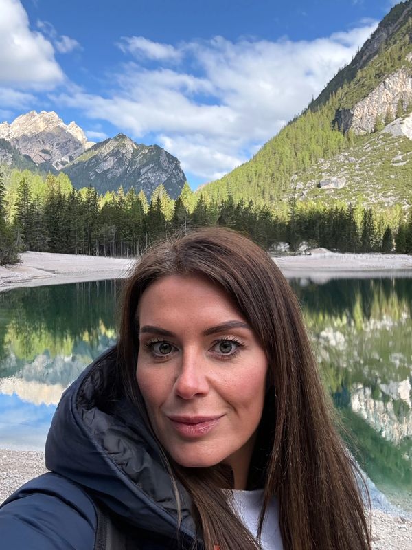 Woman taking a selfie by a serene mountain lake with clear reflections.