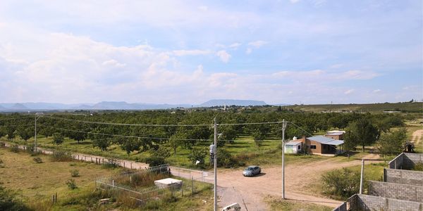 Rural landscape with farmland, a car, and small buildings under a blue sky.