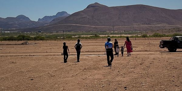 A group of people walking on a barren land with mountains in the background.
