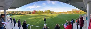 group of people standing well apart singing in the stands at local rugby club