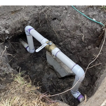 PVC pipes with a valve installed in a dug hole in the ground.