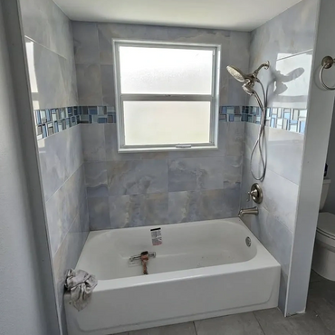 Modern bathroom with bathtub, tiled walls, and a frosted window.