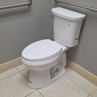 A clean white toilet with safety grab bars on gray walls and tiled floor.