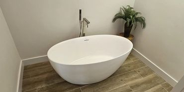 Modern bathroom with a freestanding white bathtub and wooden floor tiles.