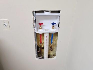 Exposed laundry water valve box with red and blue handles.