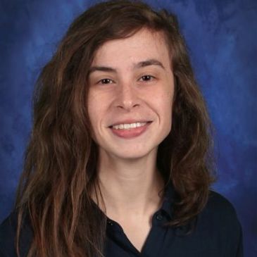 Young woman with long hair smiling against a blue backdrop.