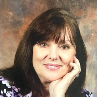 Smiling woman with dark hair resting her face on her hand.