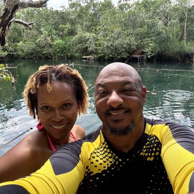 Smiling couple takes a selfie by a serene forest lake.