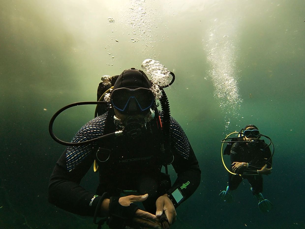 Two scuba divers exploring underwater with bubbles rising above them.
