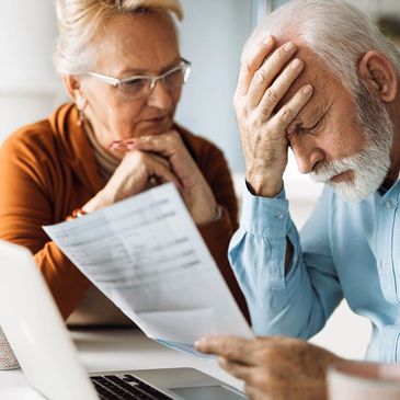 Elderly man stressed over bills as woman looks on.