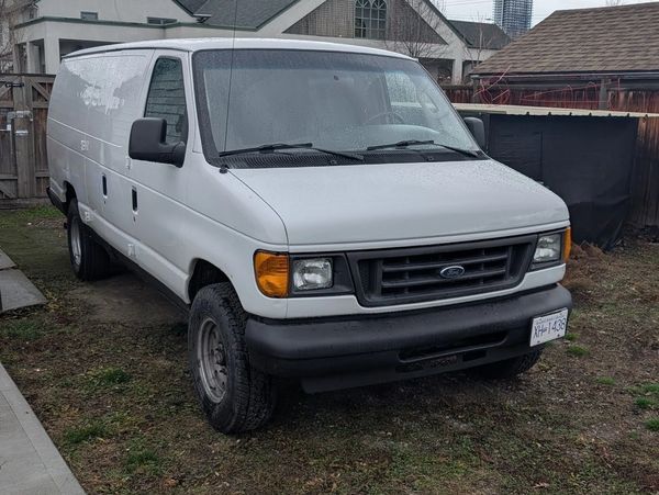 White Ford cargo van parked on grass near houses on a cloudy day.