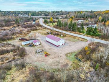 Aerial view of a rural area with buildings and machinery surrounded by trees.