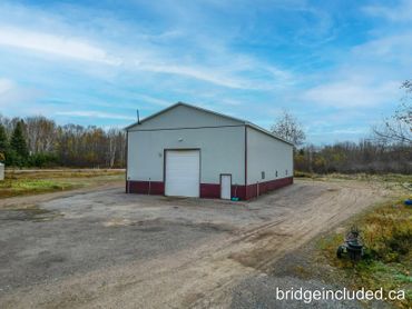 A large white and maroon industrial building in a rural area under a blue sky.