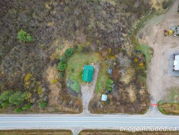 A small green-roofed house surrounded by trees and a road at the bottom.
