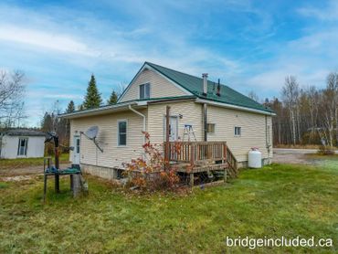 A beige house with a green roof in a grassy yard under a blue sky.