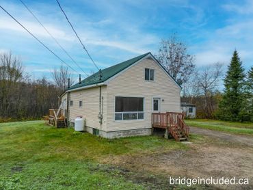 A beige house with green roof in a grassy area under a blue sky.