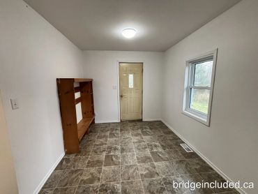 Empty room with tiled floor, white walls, a wooden shelf, and a door.