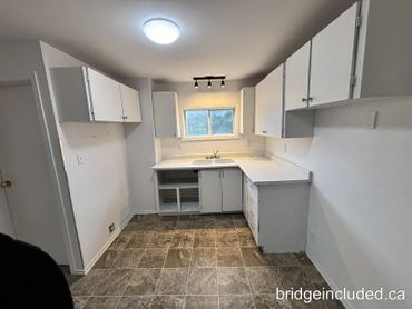 Empty kitchen with white cabinets, tiled floor, and a small window above the sink.