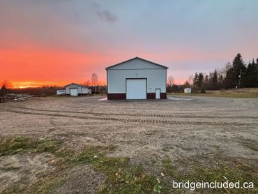 Sunset over two industrial buildings in a rural area.