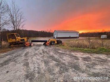 Construction vehicles blocking a gravel road at sunset.