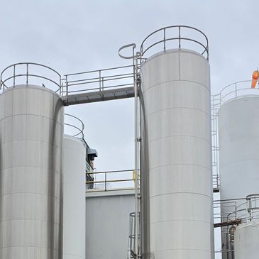 Tall industrial storage silos connected by a walkway under a gray sky.