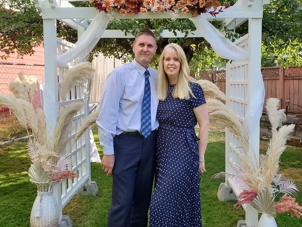 Couple posing under a decorated white arch in a garden.