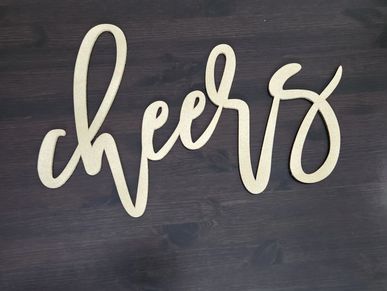 Decorative golden word "cheers" on a dark wooden surface.