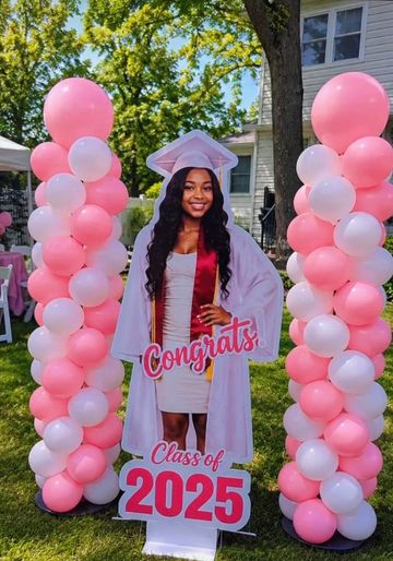 Graduation celebration setup with pink and white balloons and a life-size cutout of a graduate.