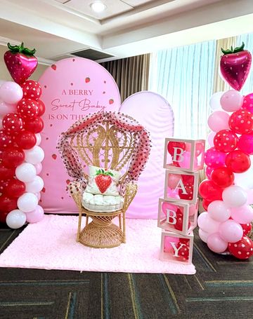 Strawberry-themed baby shower setup with balloons and a decorative chair.