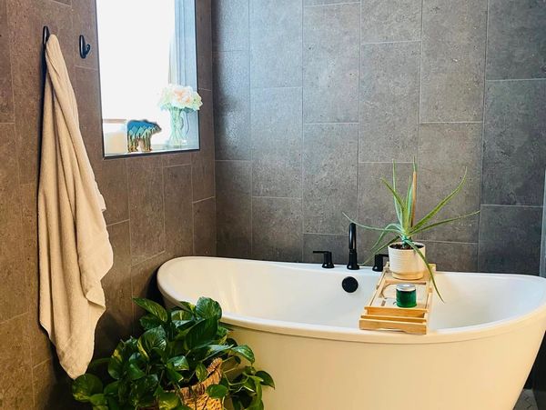 Modern bathroom with a white bathtub, plants, and gray tiled walls.