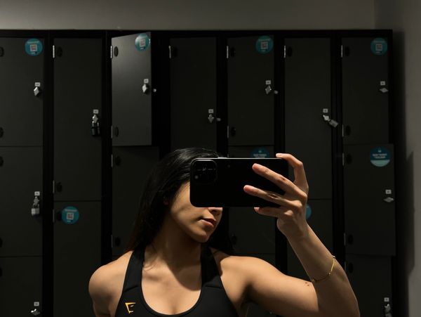 Woman taking a selfie in a gym locker room with black lockers.