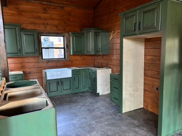 Kitchen under construction with green cabinets and wooden walls.