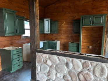 Unfinished kitchen with green cabinets and wooden walls.