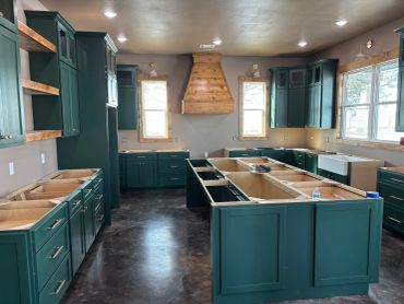 Kitchen with dark green cabinets and wooden accents under construction.