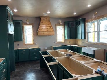 Kitchen under construction with green cabinets and wooden accents.